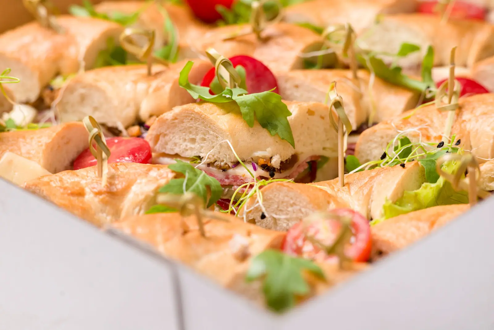 Assorted catering sandwiches with greens, tomatoes and cheese packed in a white catering box