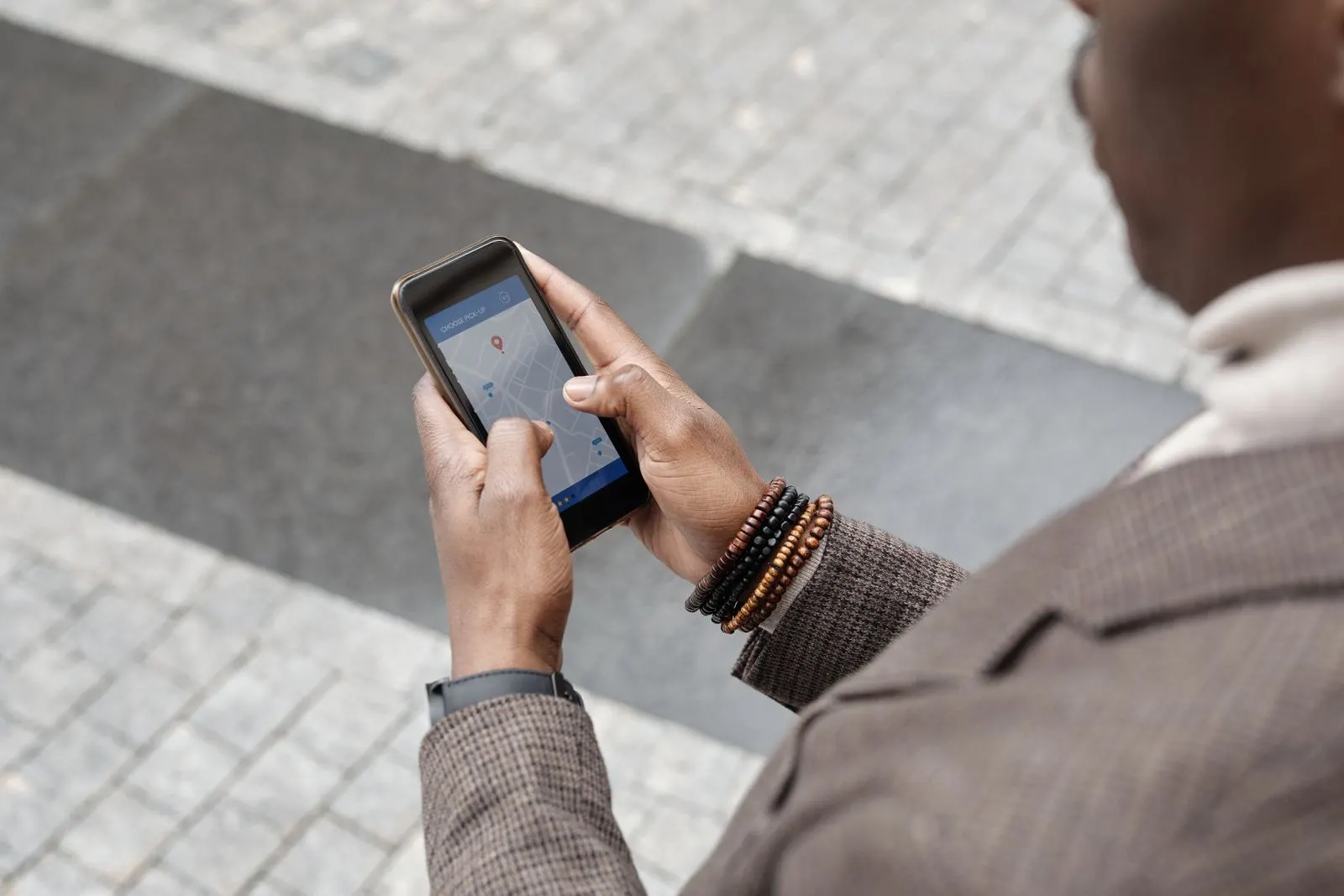 Person on a city sidewalk choosing a pickup point on a map in a phone app