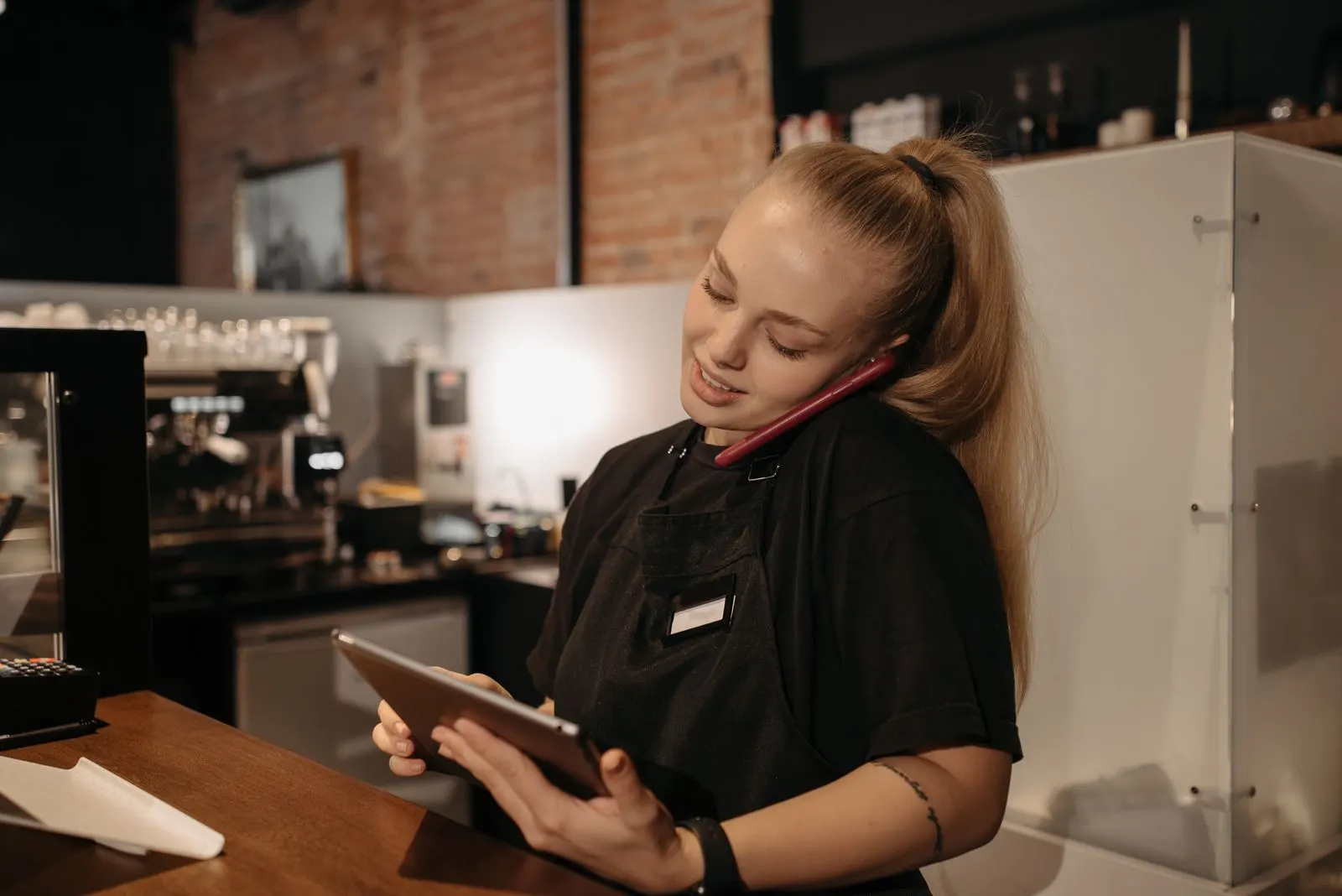 Restaurant worker at the counter checking orders on a tablet while taking a phone order