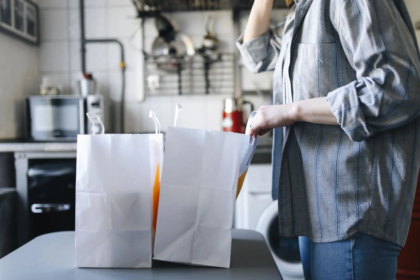 Restaurant worker packing two white takeout bags on a kitchen counter, ready for a delivery courier